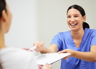 Woman in blue scrubs smiling taking paperwork from patient