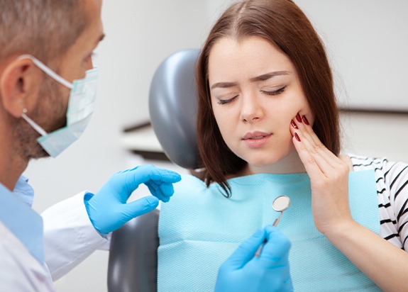 Young woman in need of pulp therapy holding cheek