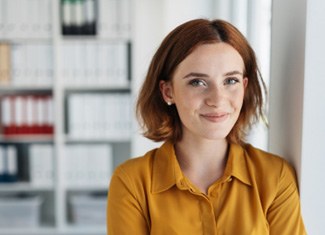 Woman in orange shirt smiling while resting against the wall