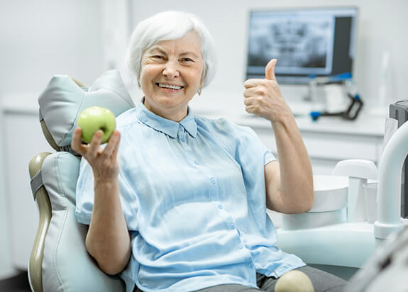 elderly woman giving a thumbs-up and holding a green apple