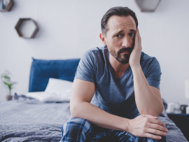 Man sitting on bed holding cheek in pain