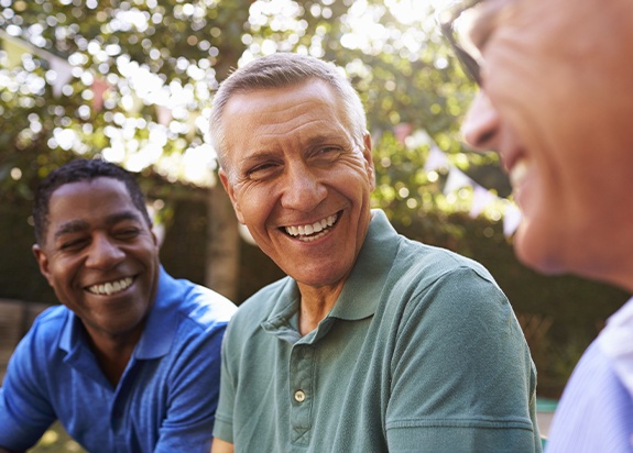 Older man smiling with friends after dental implant tooth replacement