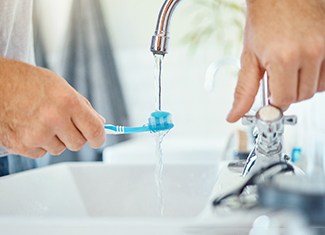 Closeup of patient turning on faucet to dampen toothbrush bristles