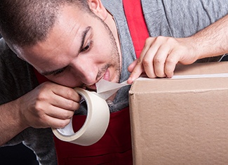 Man using his teeth to cut tape on box