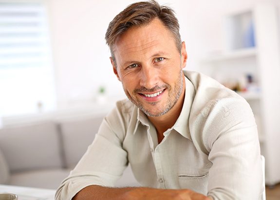 Man in off-white shirt sitting at table and smiling