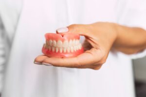 Woman wearing white holding a full set of dentures in her hand