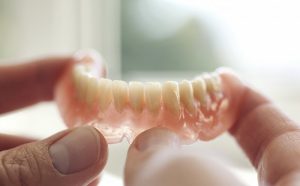 Person holding set of dentures near a window