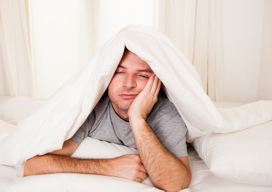 Man laying in bed under blanket looking tired and fed up