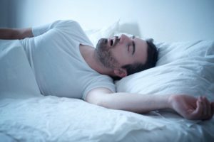 Man snoring in bed because of his sleep apnea.