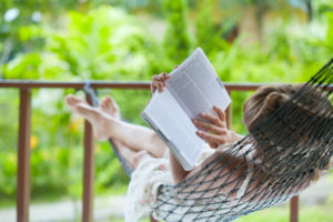 Woman lying in hammock in backyard, reading