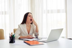 woman who needs sleep apnea therapy in Fresno yawning at her desk 